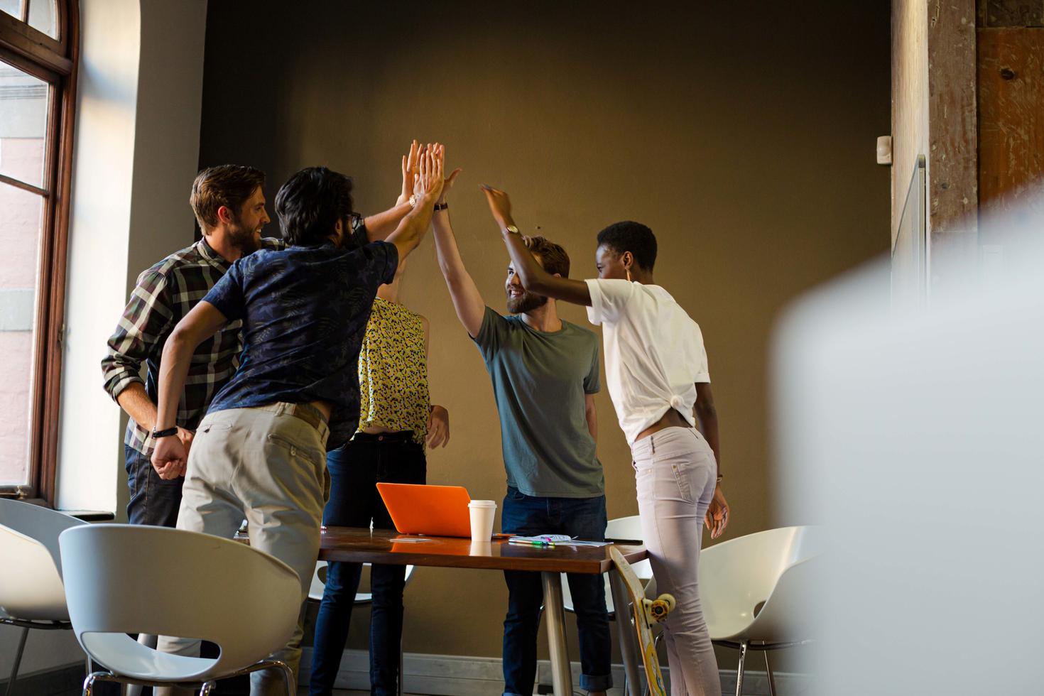 Casual business people raising hands in circle in sunny office meeting