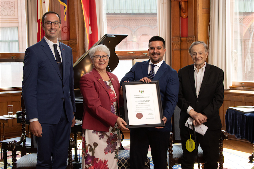 An award winner holding a plaque alongside three individuals
