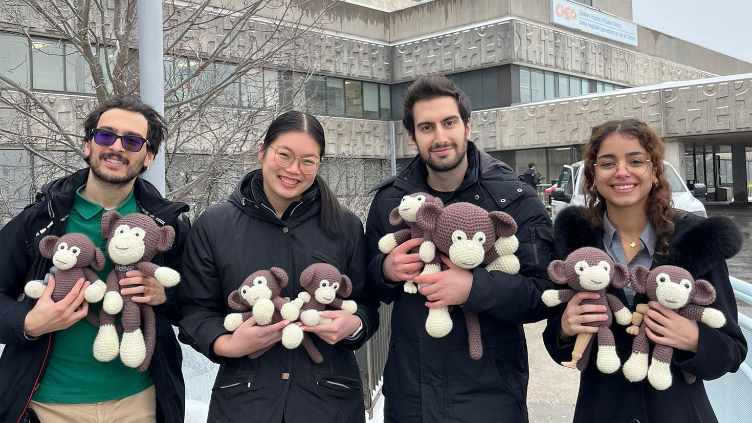 4 Faculty of Medicine students in front of CHEO holding crocheted monkeys they made for patients at the hospital