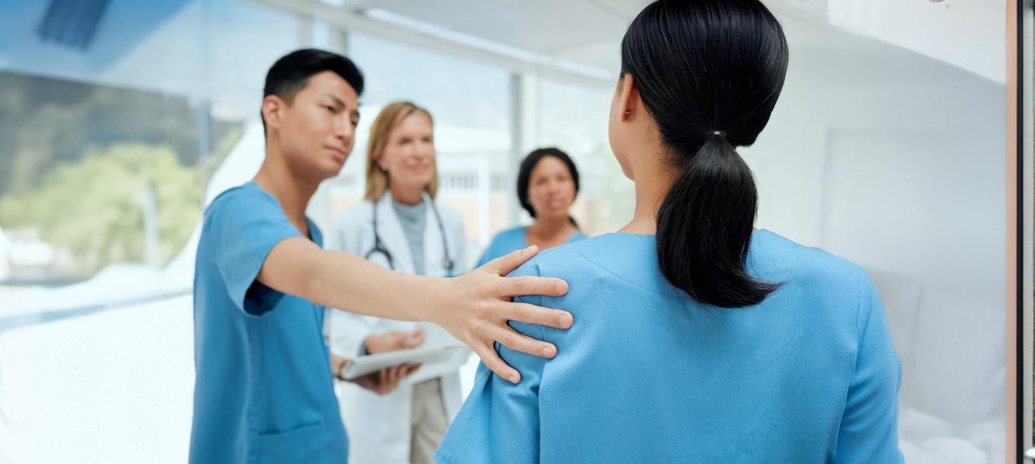 A healthcare worker comforting a colleague while two doctors talk in the background.