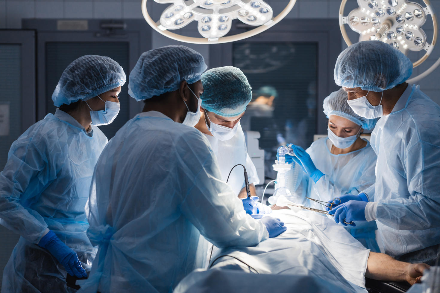 Medical professionals wearing surgical gowns, masks, and gloves work together during an operating room procedure