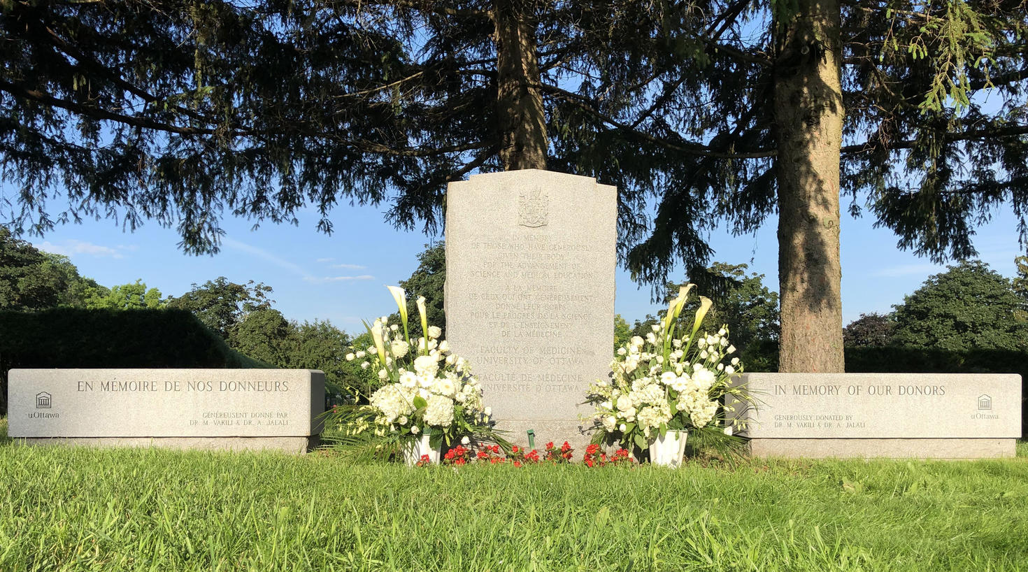 Pinecrest Cemetery Memorial stone adorned with flowers with two stone benches on either side.
