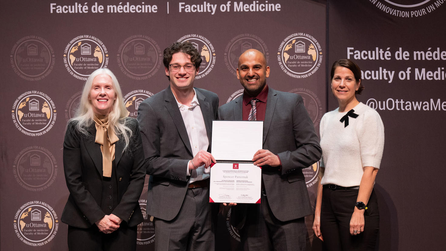 An award winner stands with a certificate alongside three faculty leaders