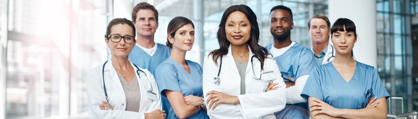 A group of healthcare professionals in scrubs and lab coats stand together in a hospital hallway