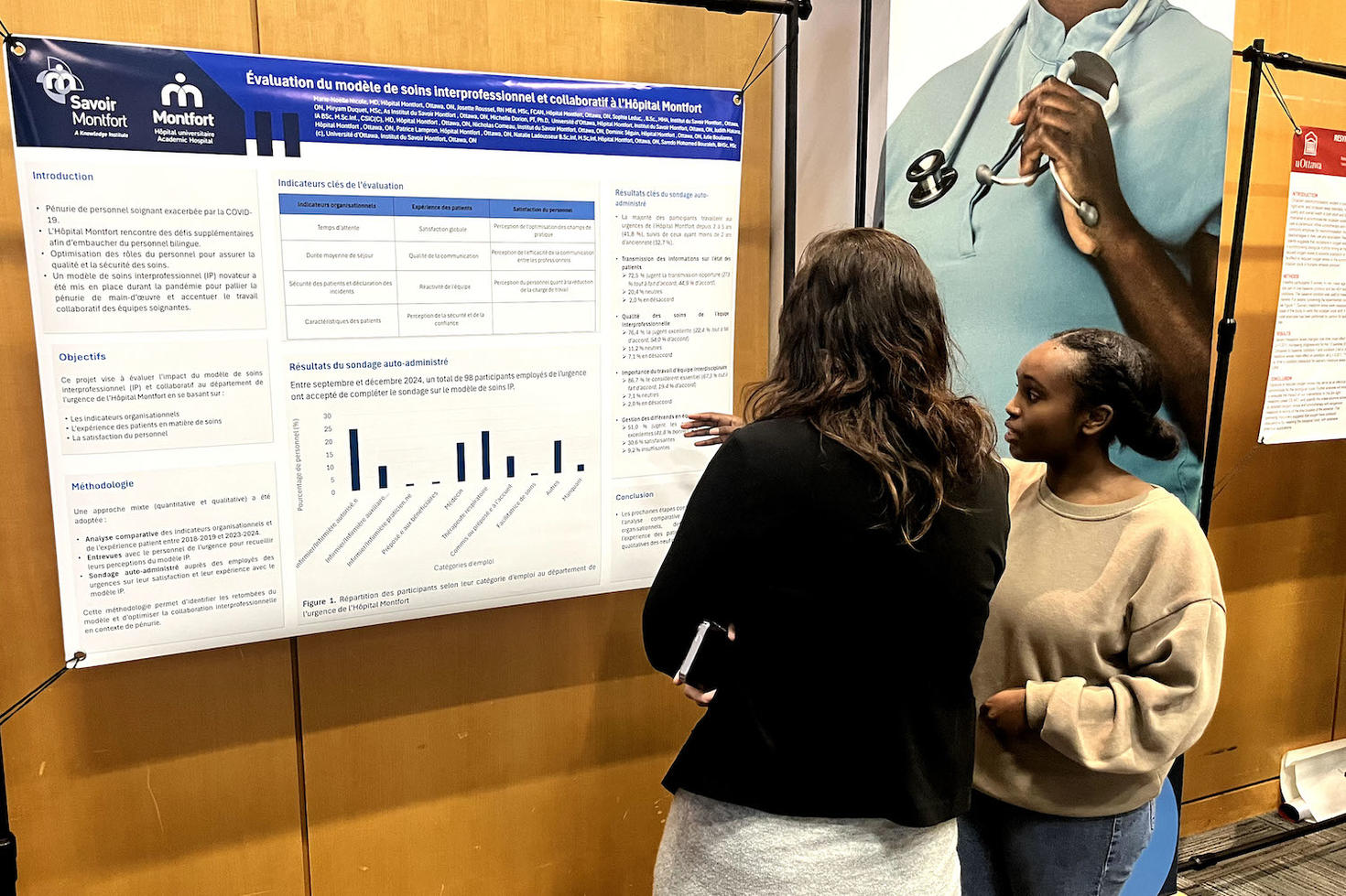 A student researcher (woman) explains her research poster to an onlooker.