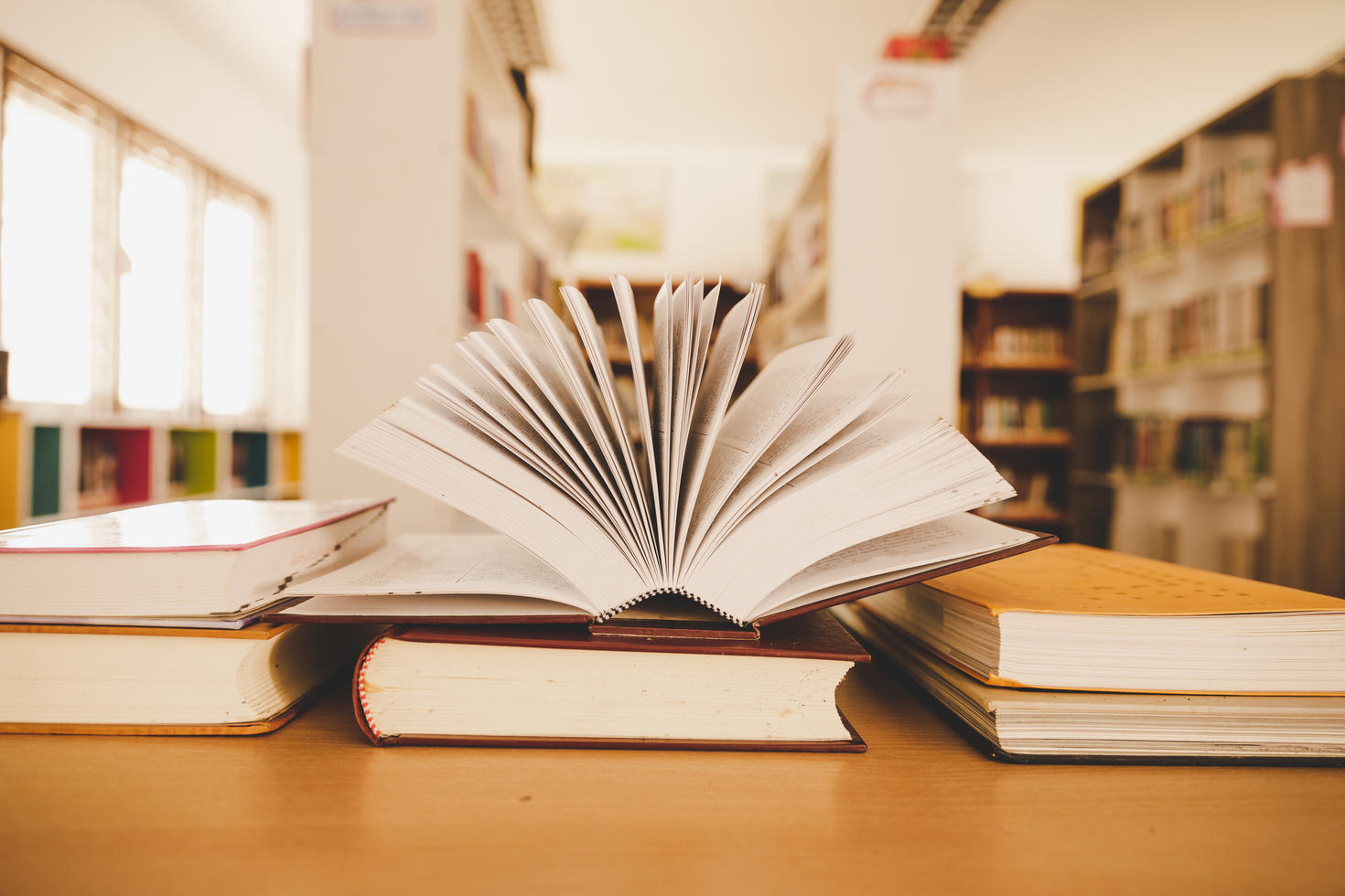 An open book resting on a stack of books in a library, symbolizing access to academic resources.