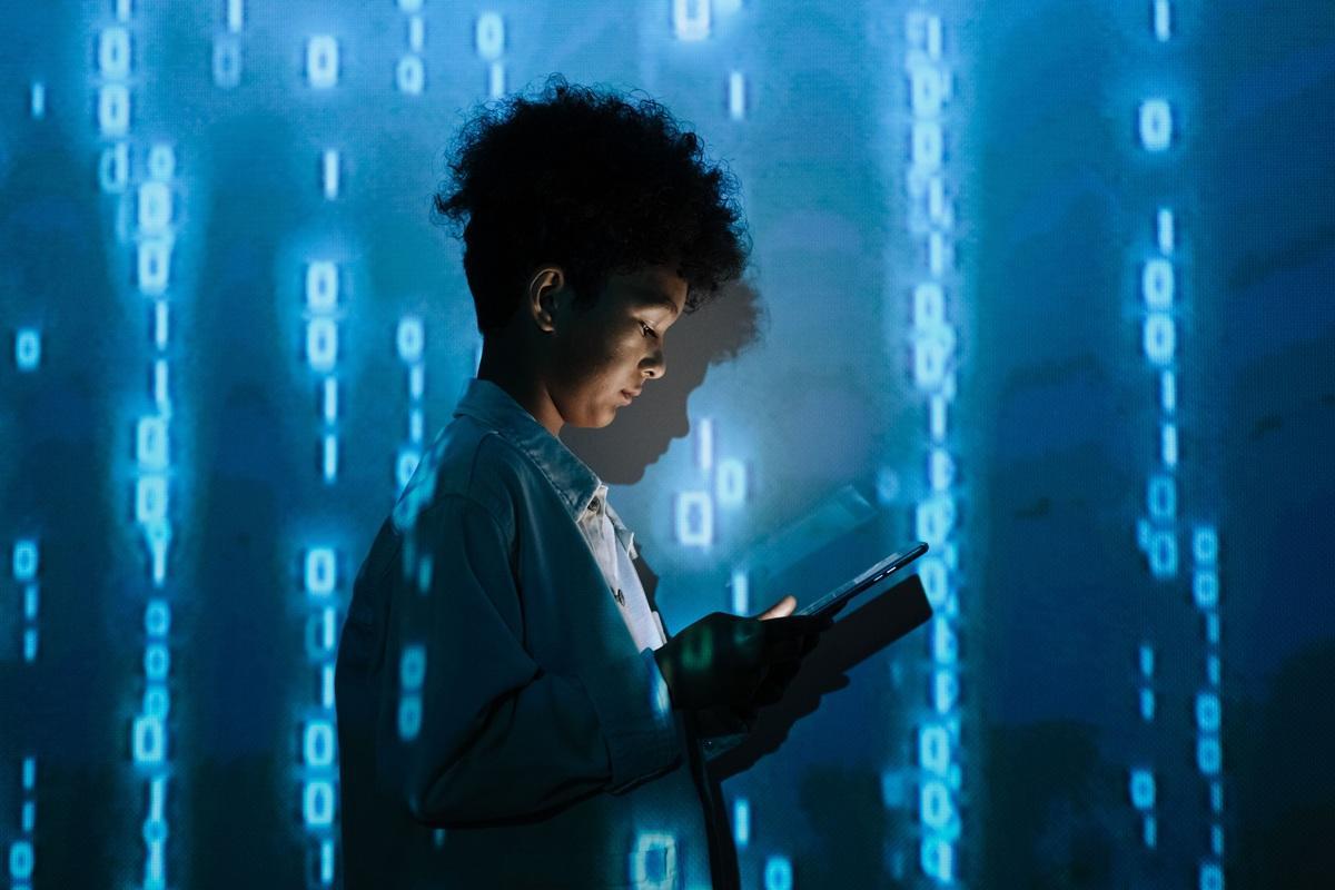 A young person in a lab coat looking down at a tablet as digital ones and zeros rain down around them