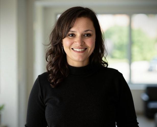 Dr. Kheira Jolin-Dahel wearing a black turtleneck sweater over a blurred clinical background