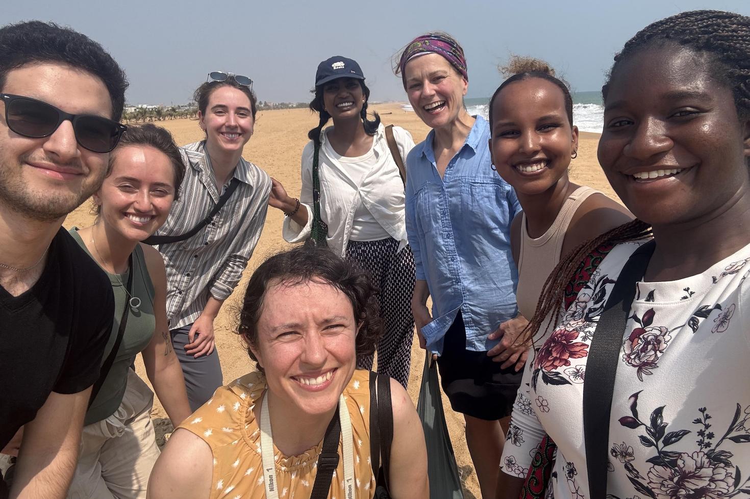 Eight learners and teachers posing together in an international, sandy location