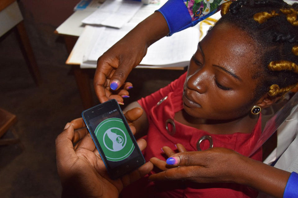 A community health worker trains a woman on how to use an app on her phone.