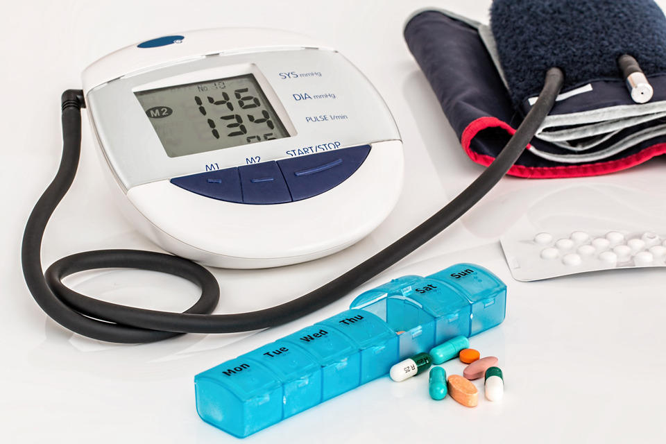 a blood pressure monitor next to a pile of medications