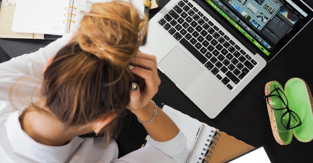 Person holding her head in front of a laptop