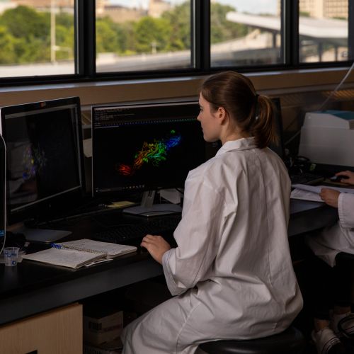 Female student wearing a labcoat and looking at date on a computer screen.