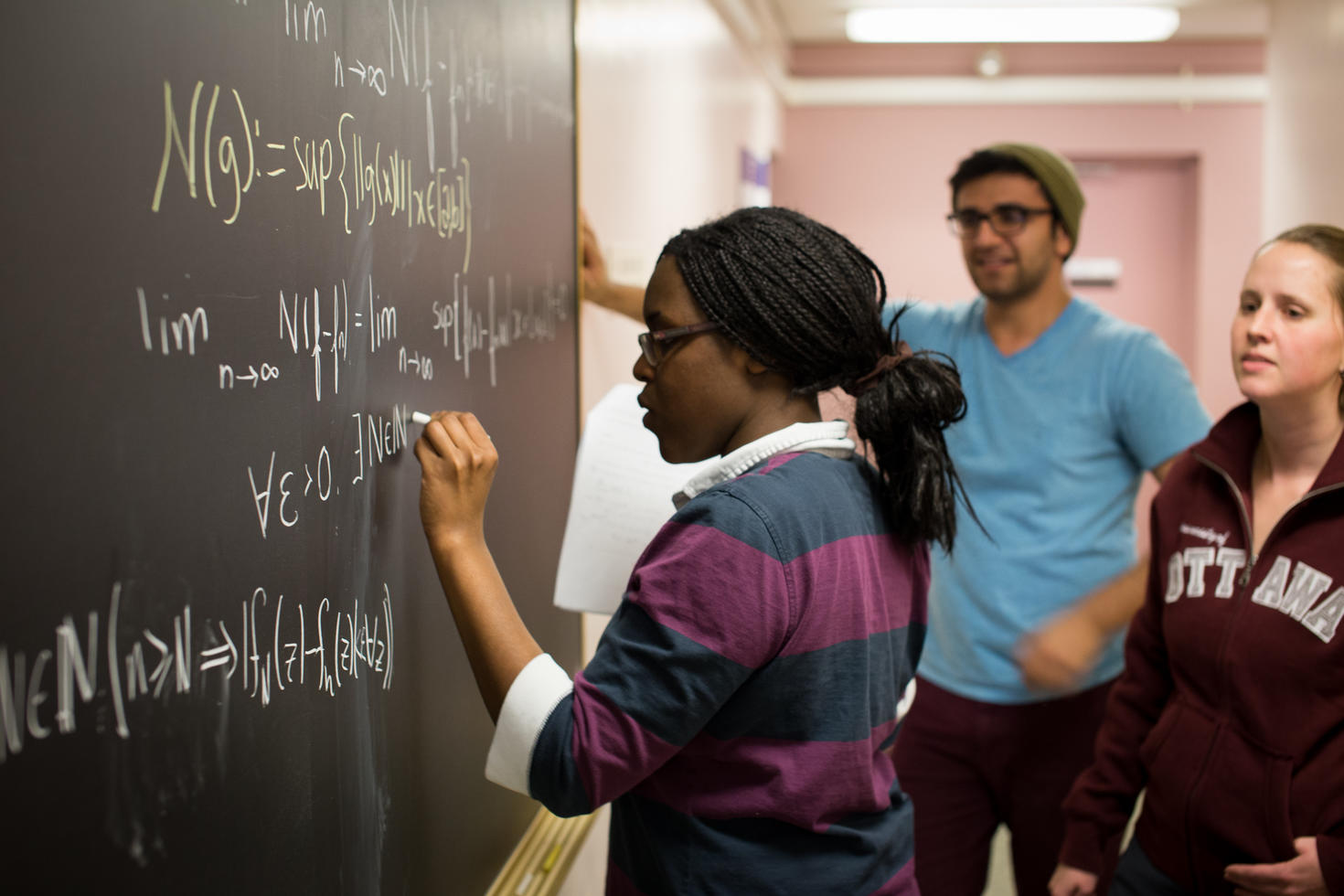Female student writing solving an equation on a board. 