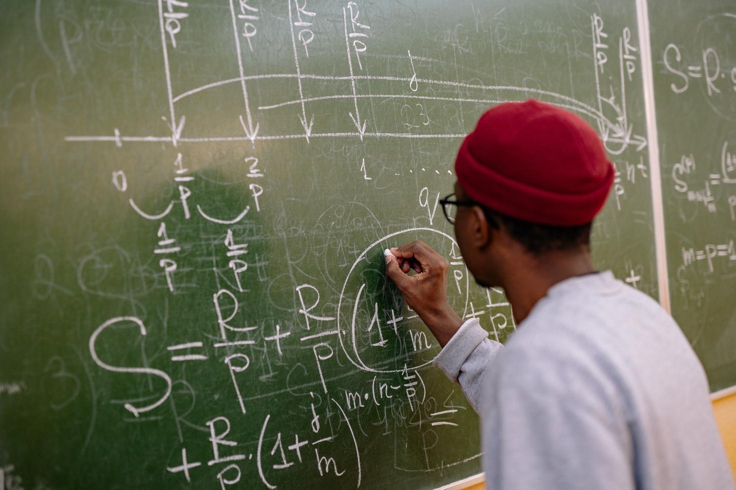 Black male student is wrighting matematical equations on a black board