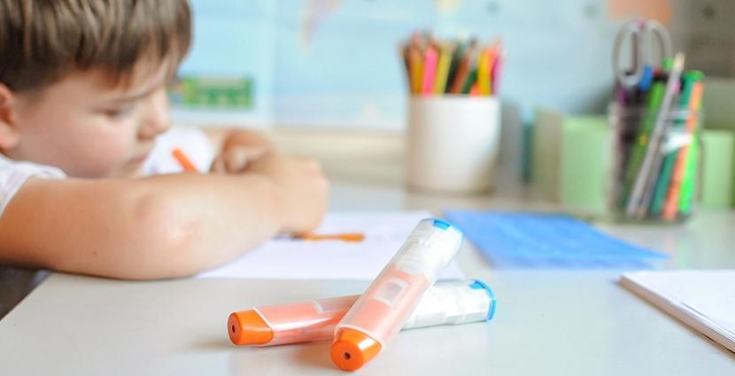 Student writing on paper and 2 epipens are on his desk