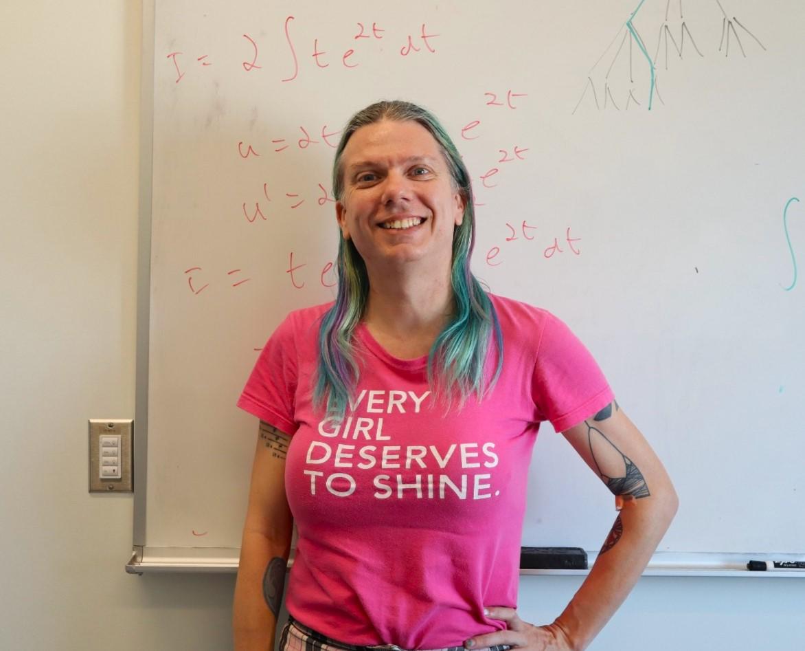 Professor Stacey Smith? stands in front of a whiteboard on which we see mathematical formulas written in red marker.