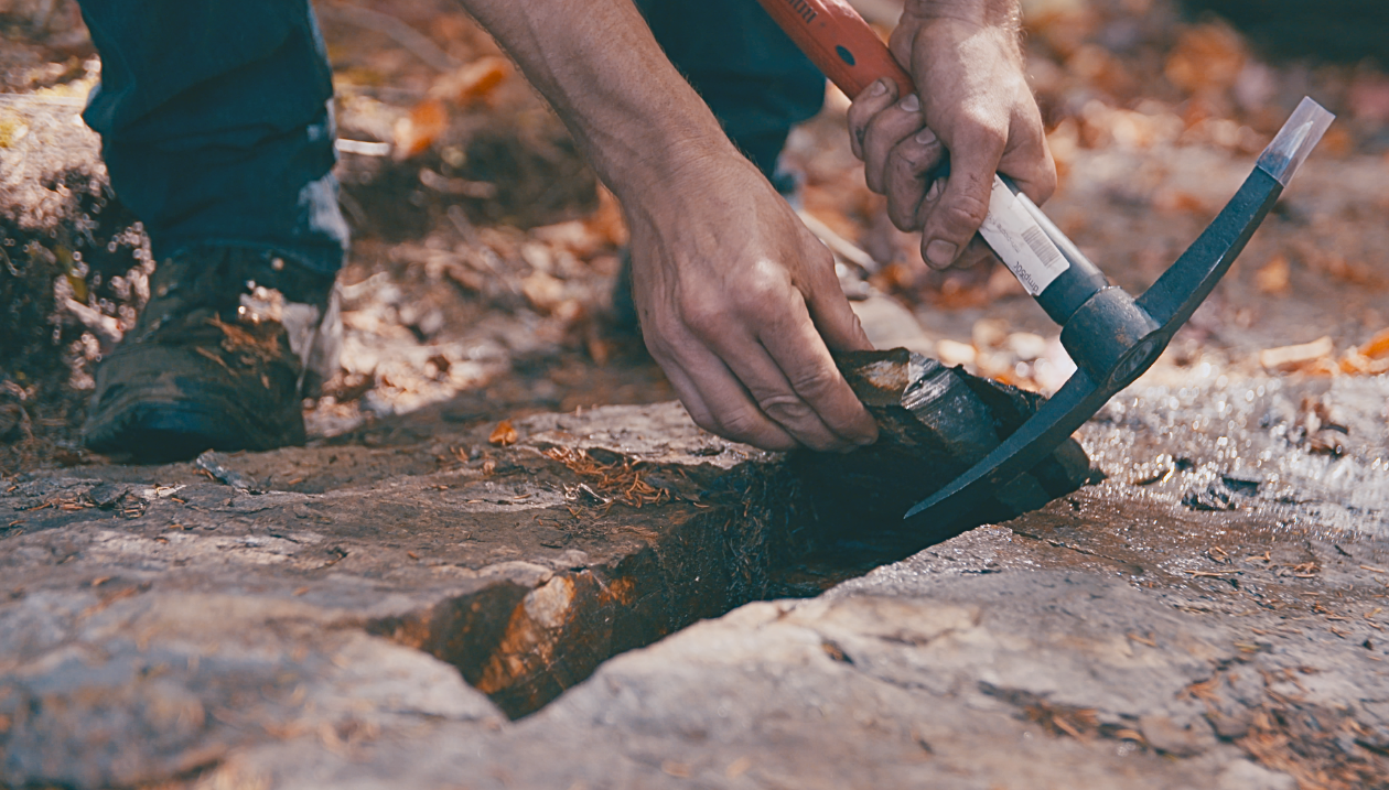A person using a geological hammer to examine a rock.