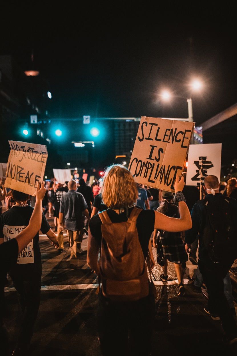 Protestors carrying signs: "No justice, no peace" and "Silence is compliance".