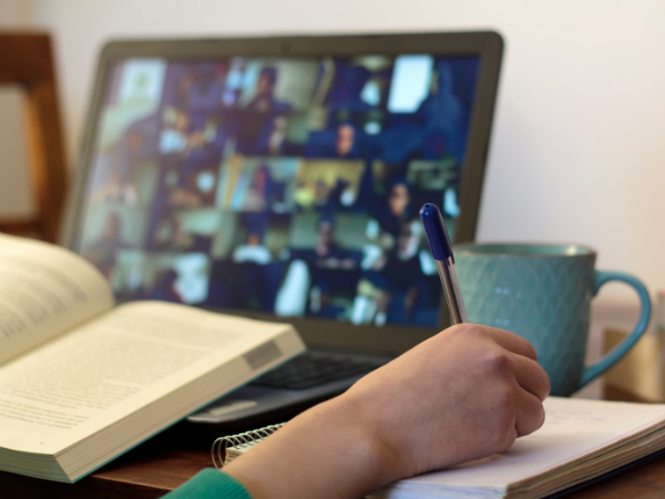 hand writing in a book in front of a laptop