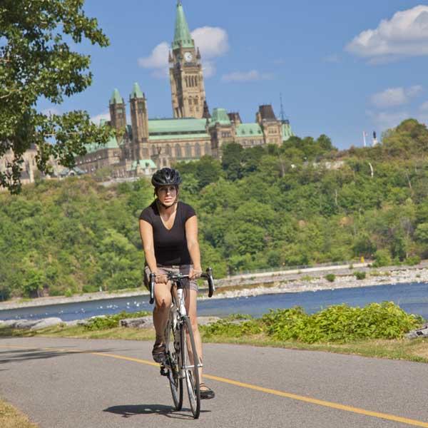 A person cycling on a bike path with the Parliament of Canada in the background
