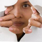 Person using hands to tear through a paper barrier and look through at us.