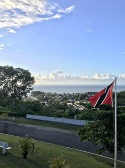 Trinidad and Tobago flag on the right side of the foreground. A road on the side along with the sky and the sea in the background