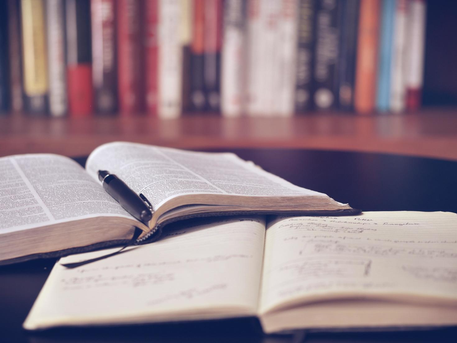 open book with pen on top of notebook in library