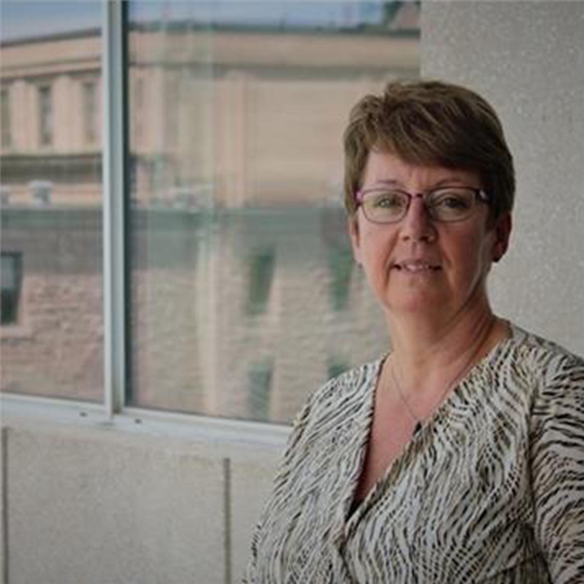 Guylaine Renaud standing by a large window with a blurred urban background.