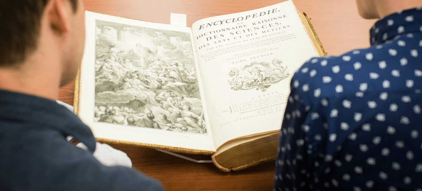 Two students, wearing gloves, looking at a book.