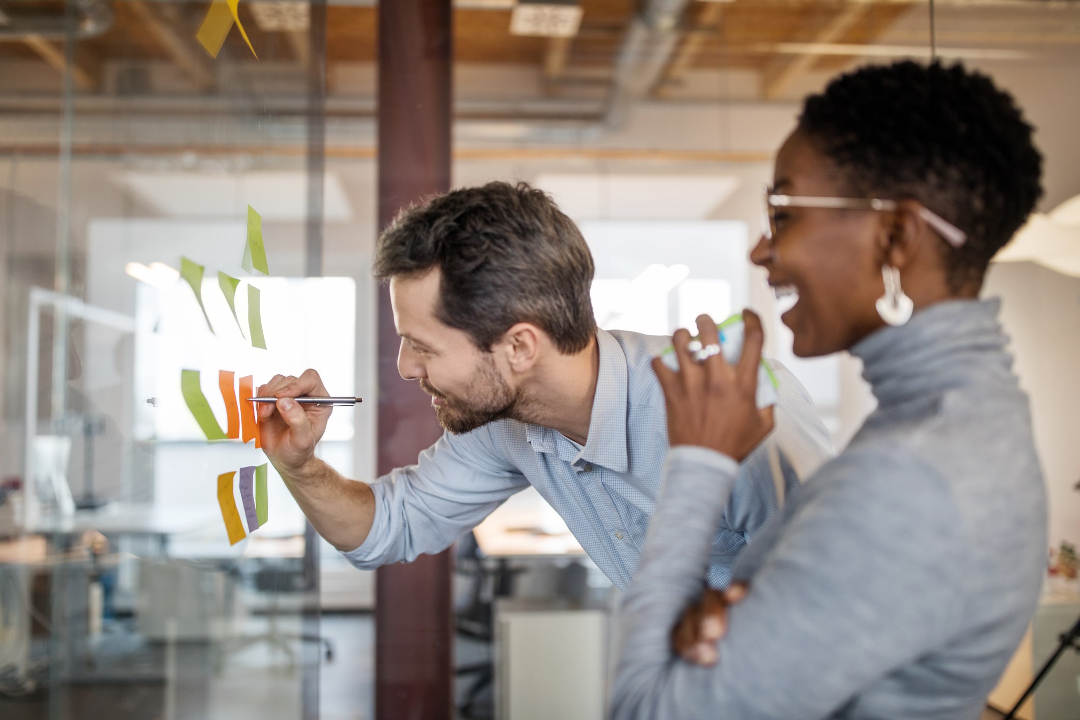 Collègues faisant un brainstorming à l'aide de post-it sur un mur de verre.