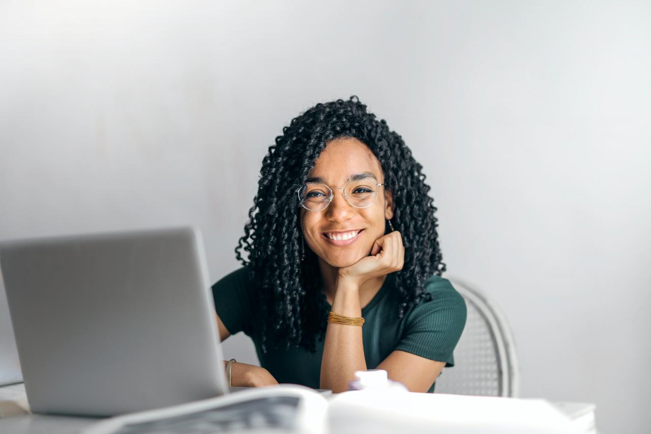 Personne souriante assise à un bureau devant un ordinateur portable.