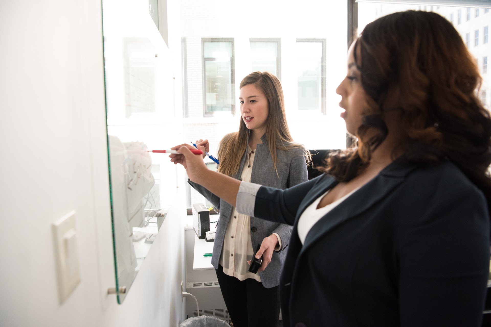 deux femmes collaborant devant un tableau blanc