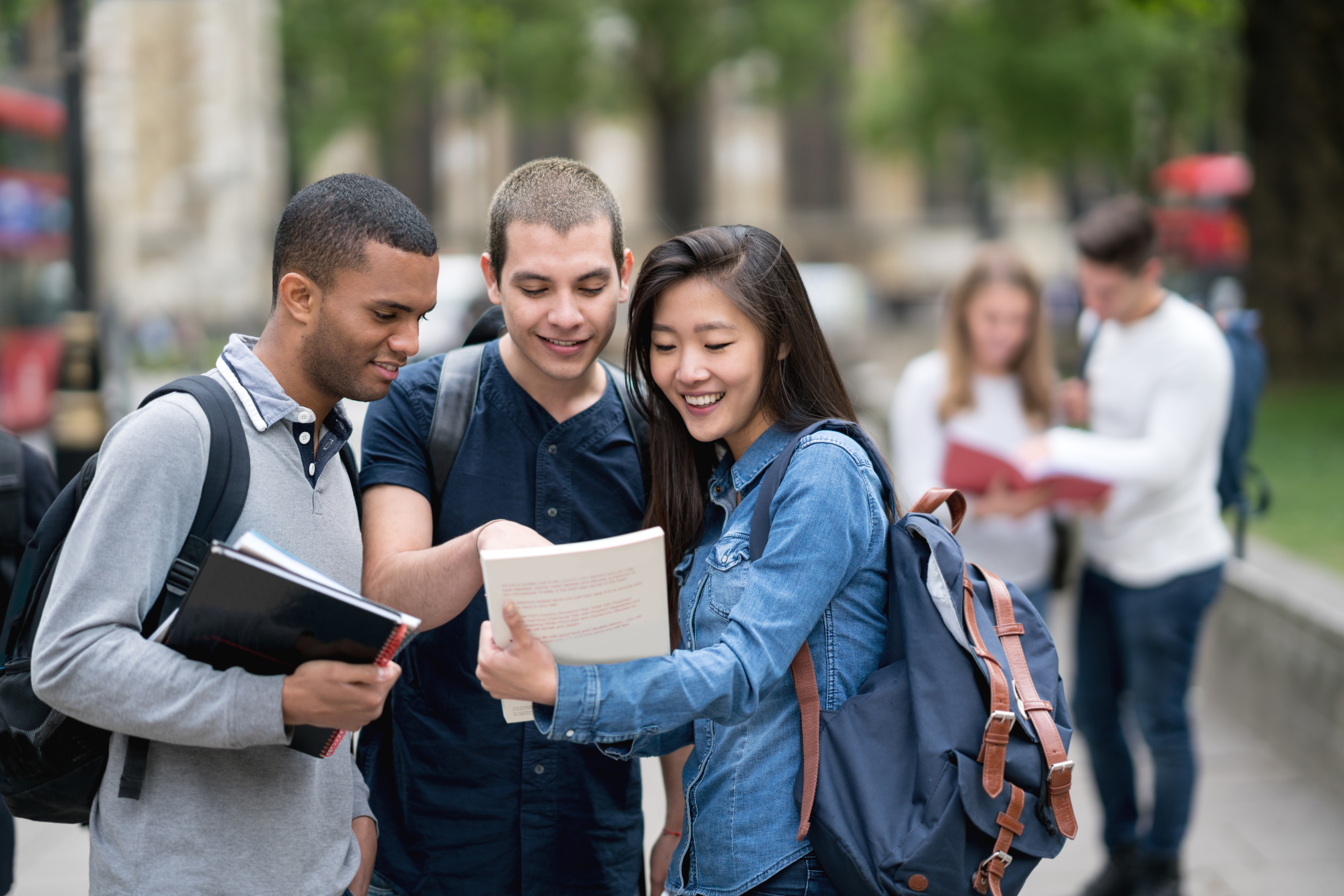 Trois étudiants debout à l'extérieur et regardant un livre