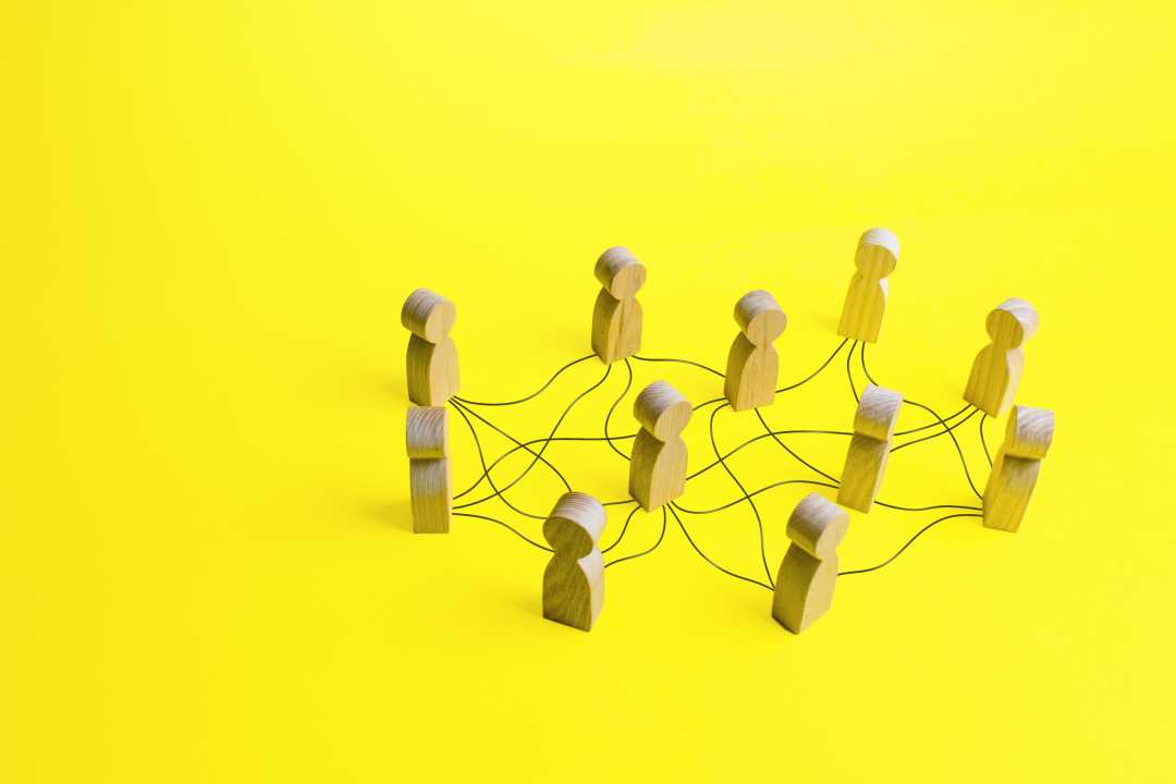 Un groupe de pièces en bois en forme humaine reliées par une ficelle rouge sur un fond jaune