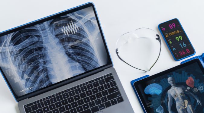 Un ensemble d’outils de diagnostic médical disposés sur une surface blanche, incluant un ordinateur portable, un smartphone et une tablette.