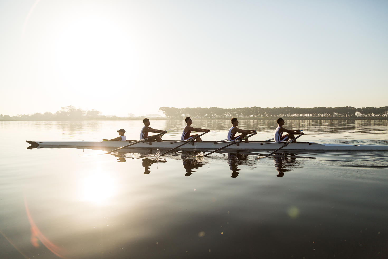 5 personnes ramant sur l'eau au coucher du soleil