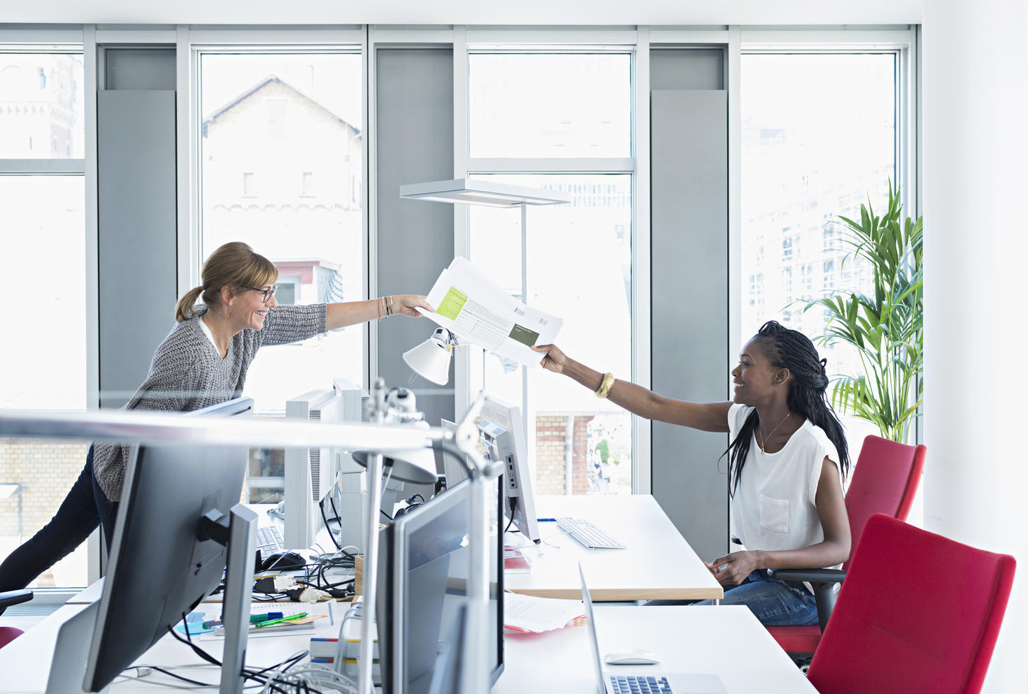 Employee handing paper to colleague over their desks.