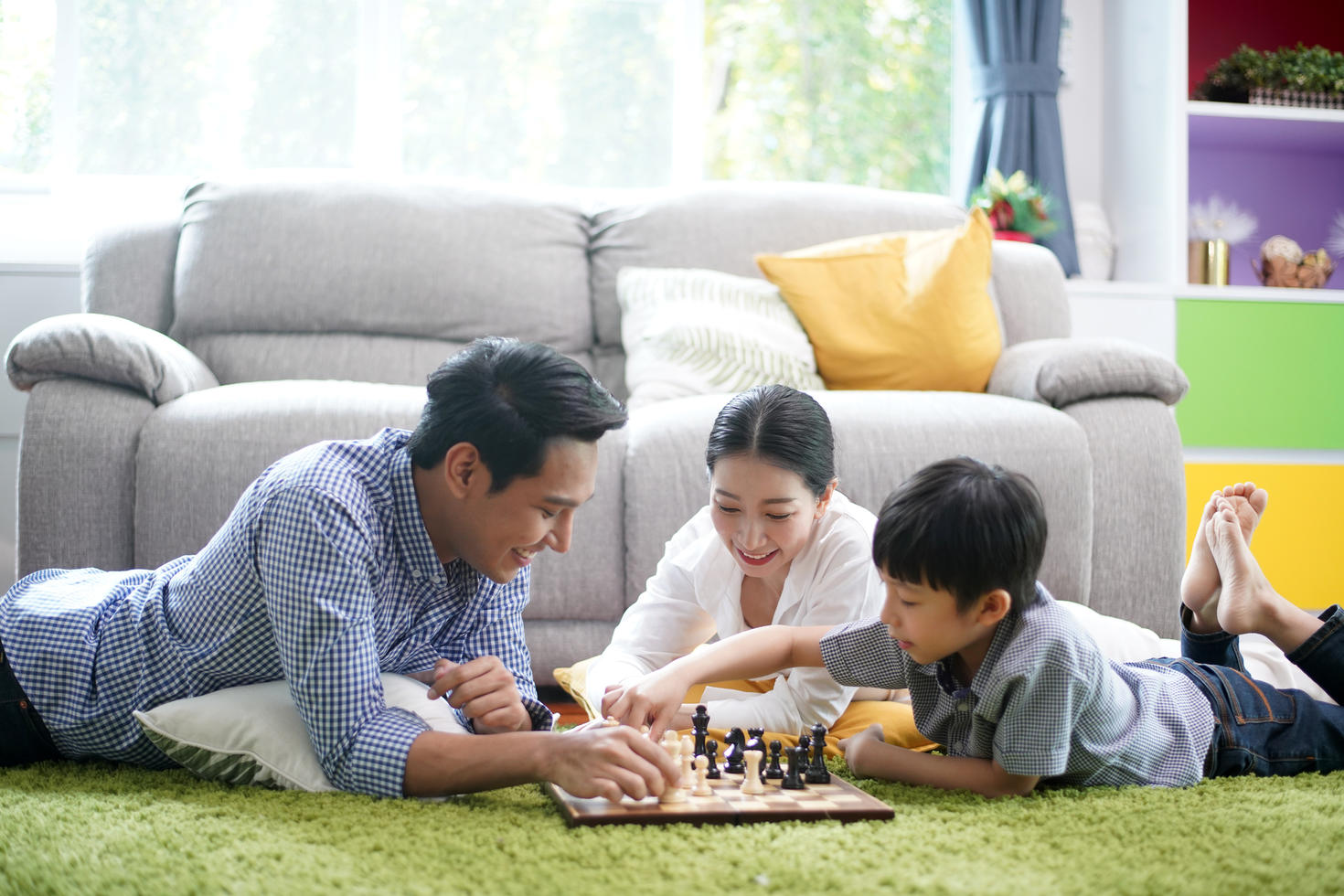 Père, mère et fils jouant aux échecs dans le salon sur un tapis.