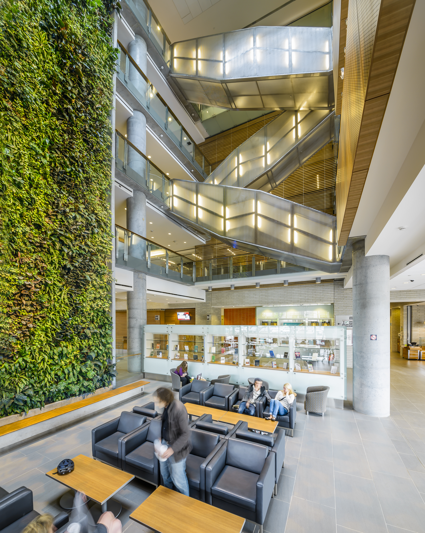 Intérieur du bâtiment du campus, avec un escalier moderne au centre et un mur de plantes vertes à gauche. 