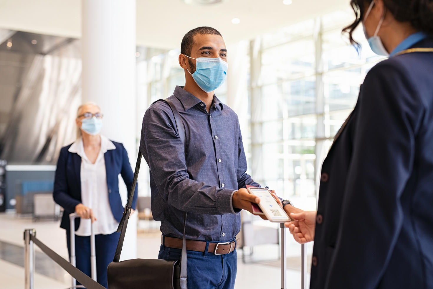 Personne dans un aéroport avec un masque montrant son billet d'embarquement.