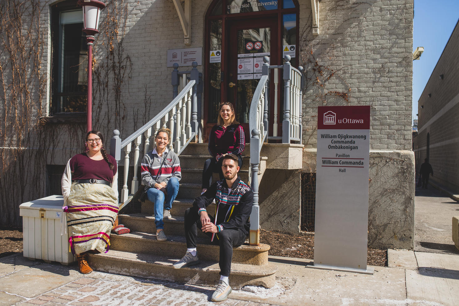 Quatre étudiants autochtones sont assis sur les marches d'un bâtiment du campus. Un panneau de l'Université d'Ottawa est visible.