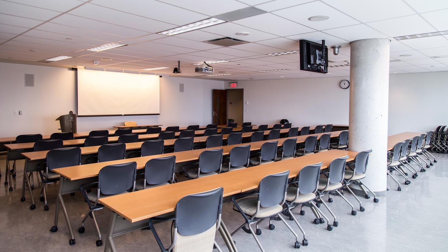 Salle Desmarais 12110, avec des bureaux, des chaises, un écran projecteur et un podium.