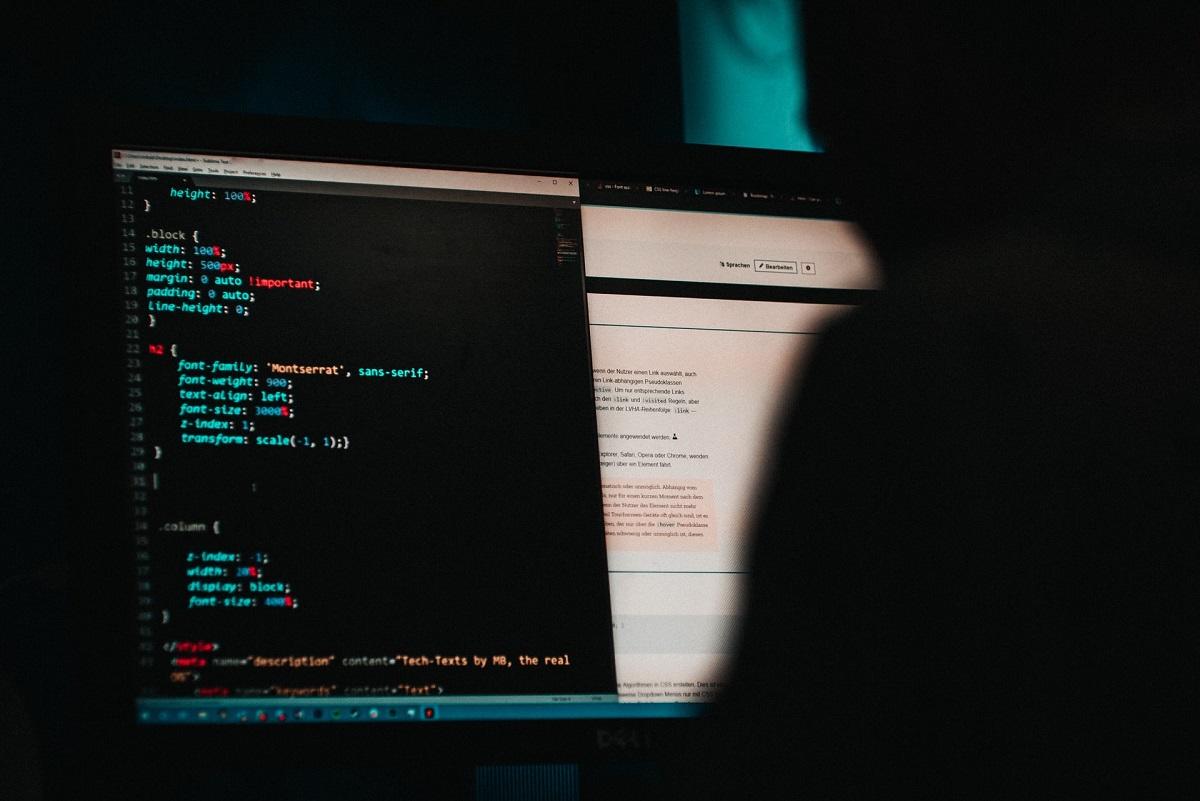 Dos d'une personne dans l'ombre dans une pièce sombre regardant un code informatique.
