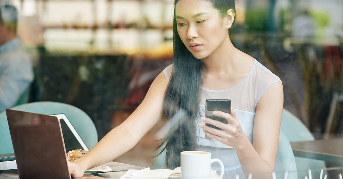 Étudiant travaillant sur un ordinateur portable et tenant un smartphone dans sa main levée