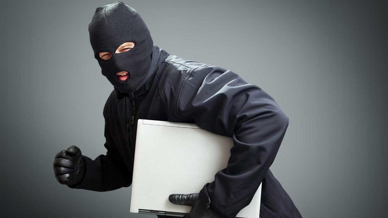 Une personne portant une cagoule vole un ordinateur portable.