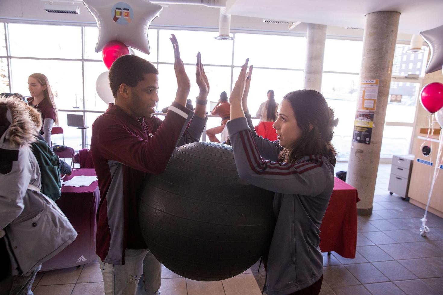Deux étudiants et étudiantes tenant un ballon entre eux sans les mains