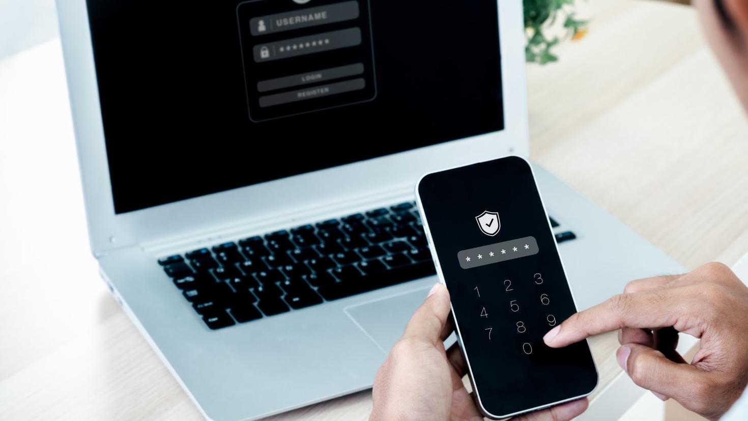 Mains tapant sur un téléphone mobile devant un ordinateur portable posé sur une table 