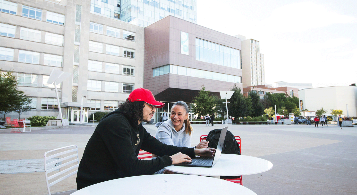 deux étudiants travaillant sur un ordinateur portable assis à une table sur la Place Université