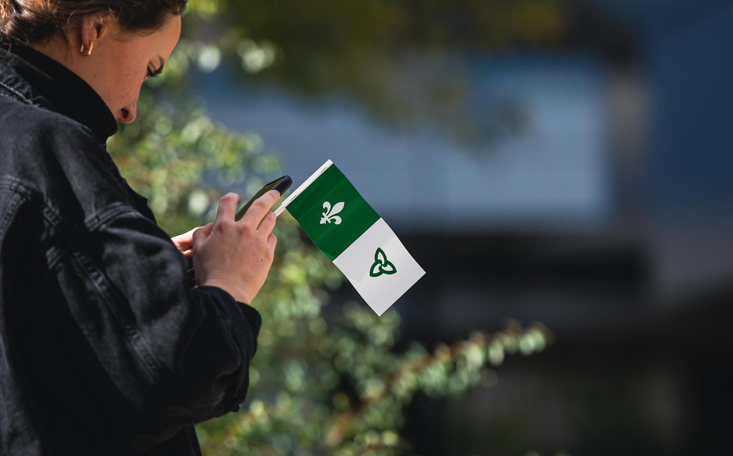 Une personne regardant son téléphone en tenant un petit drapeau de la Francophonie.